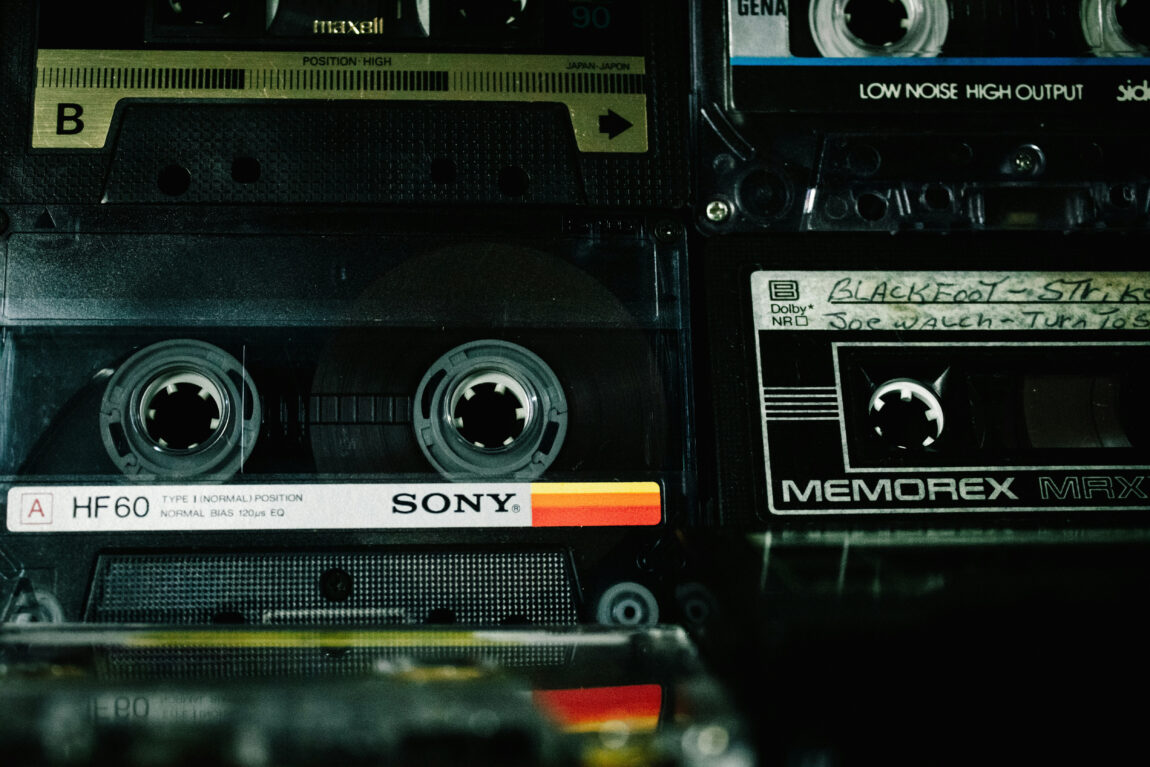 Close-up of stacked vintage cassette tapes with visible brands like Sony and Memorex. Labels show handwritten text, creating a nostalgic mood.