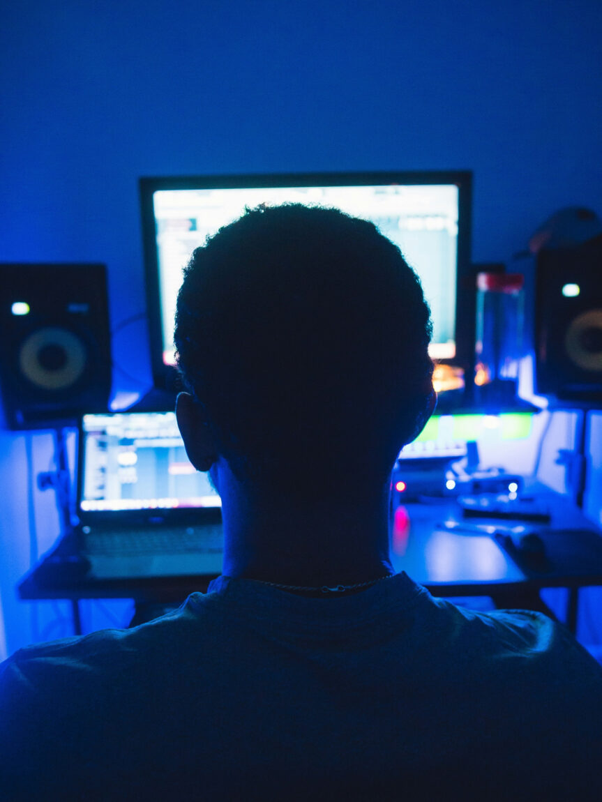 Man producing music, sitting in front of a computer monitor and laptop.